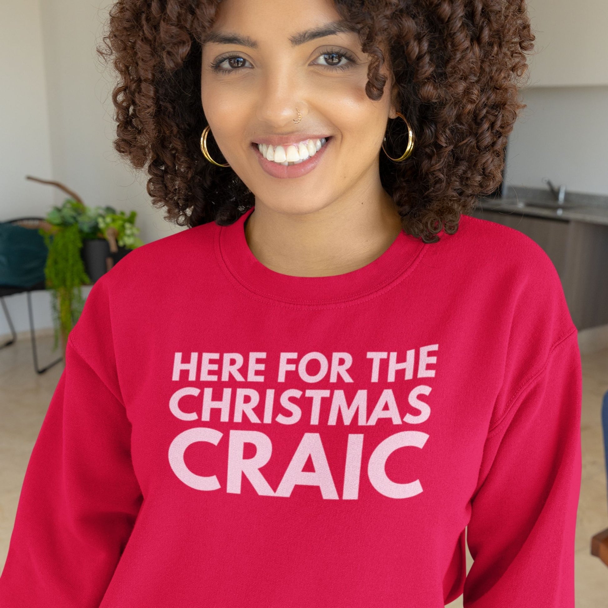 Person wearing a red sweatshirt with 'HERE FOR THE CHRISTMAS CRAIC' pink text in a kitchen setting