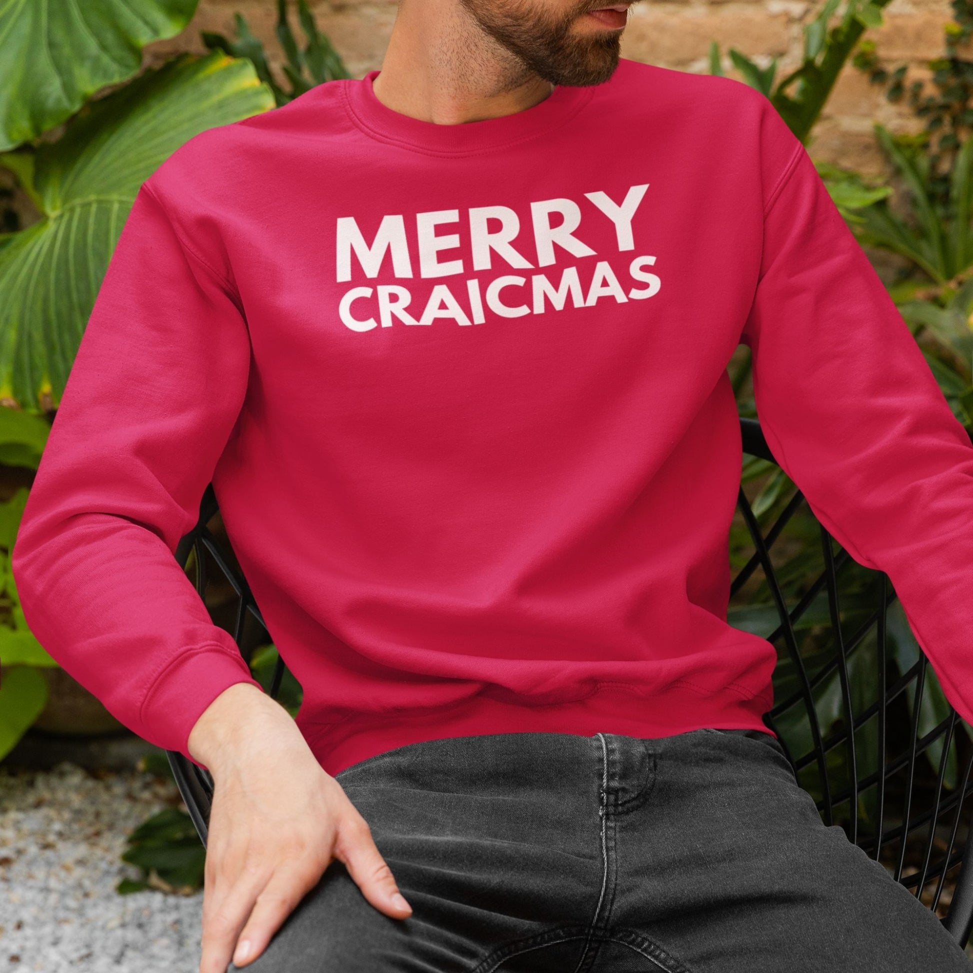 Person wearing a red sweatshirt with 'MERRY CRAICMAS' white text, sitting outdoors.