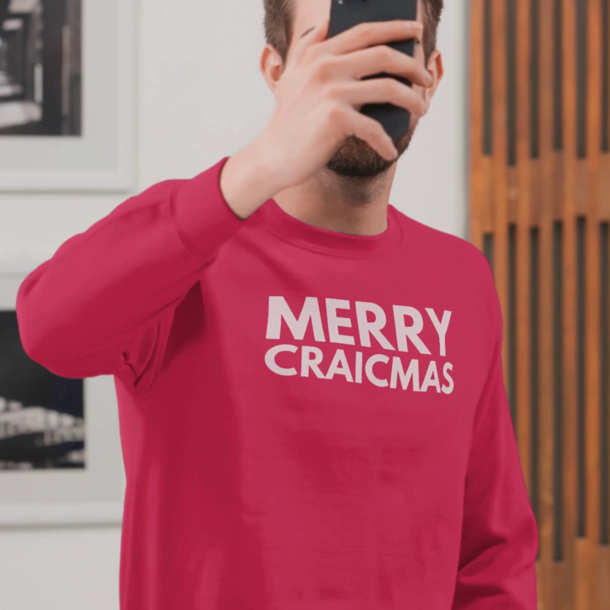 Person holding a mobile phone over their face wearing a red Christmas jumper with white text "Merry Craicmas"