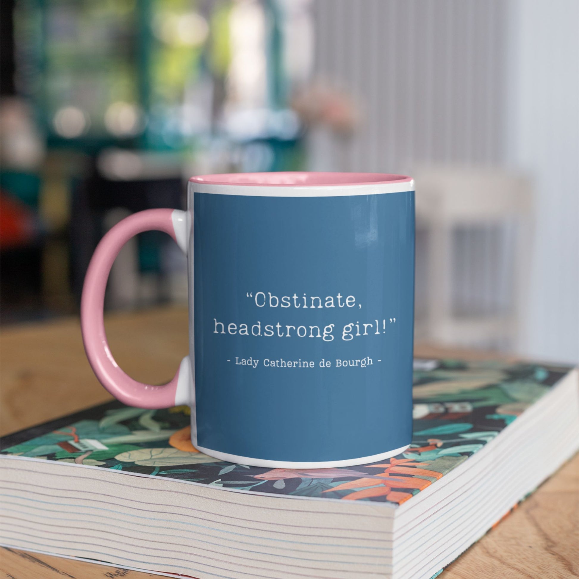 Jane Austen Pride and Prejudice blue mug with pink handle on a book, featuring text.