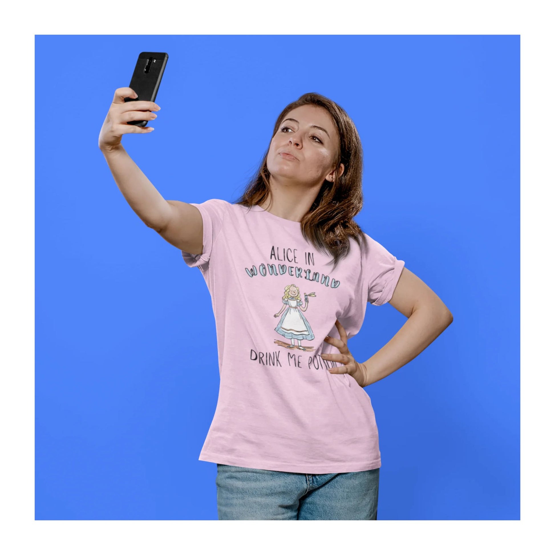 Woman wearing a pink t-shirt with a graphic design and text, taking a selfie against a blue background.
