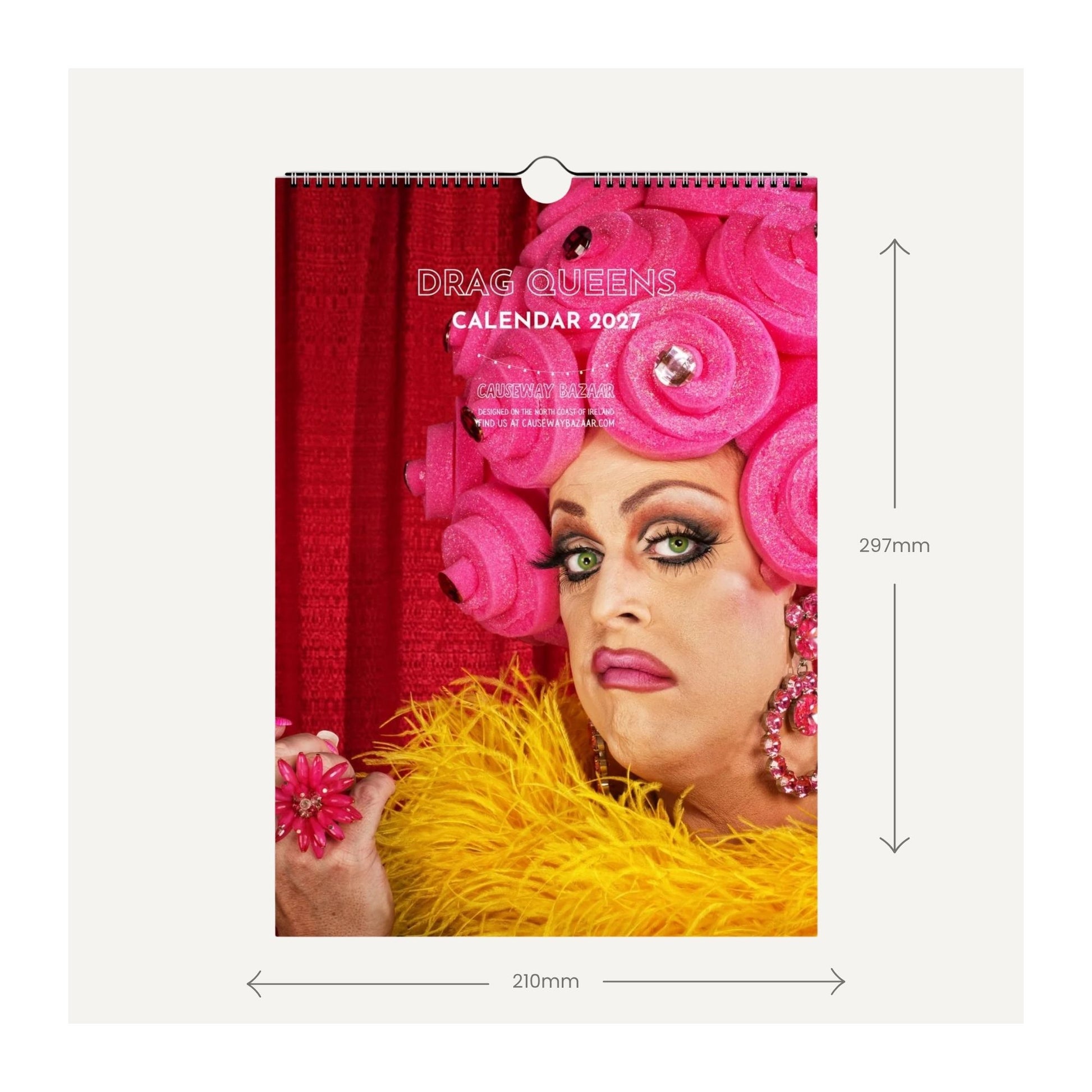 A wall calendar cover shown flat against a light grey background, with dimension arrows and labels indicating 210mm width and 297mm height. The cover features a close-up portrait of an LGBTQ person with bright pink hair, a red curtain backdrop, and a yellow feathered garment.