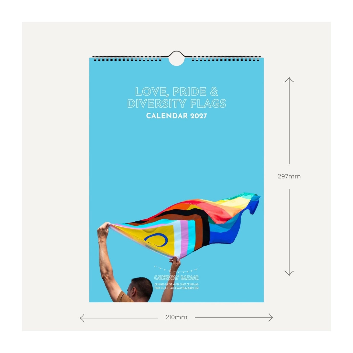 A wall calendar shown front-facing with dimension arrows and labels indicating 297mm height and 210mm width. The cover is bright blue with white text reading 'LOVE, PRIDE & DIVERSITY FLAGS CALENDAR 2027' and an illustration of a person holding a rainbow pride flag.
