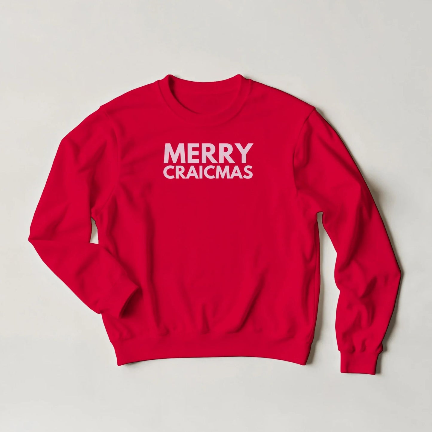 Red sweatshirt with 'MERRY CRAICMAS' text text in pink on a grey background