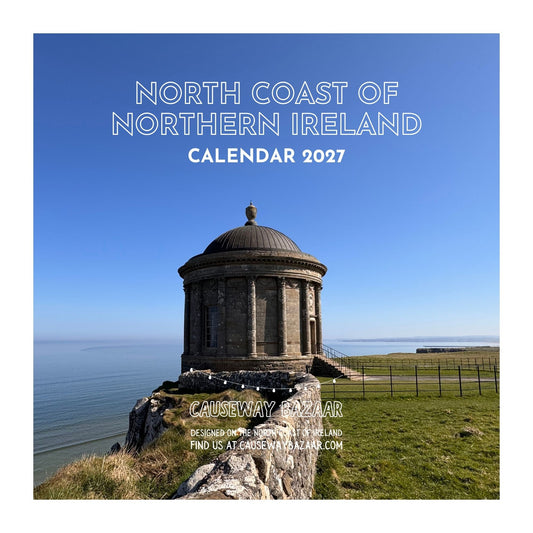 Square promotional image for a 2027 calendar titled 'North Coast of Northern Ireland Calendar 2027,' featuring a scenic photograph of a stone domed structure on a grassy cliff overlooking the sea under a clear blue sky. The text 'Causeway Bazaar' appears near the bottom with contact details.