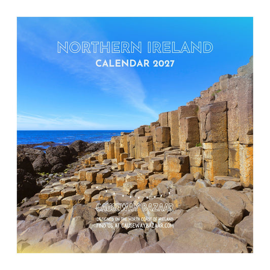 Northern Ireland 2027 calendar cover featuring a scenic photograph of the Giant's Causeway rock formations under a bright blue sky, with the title 'NORTHERN IRELAND CALENDAR 2027' and publisher text 'CAUSEWAY BAZAAR' overlaid.