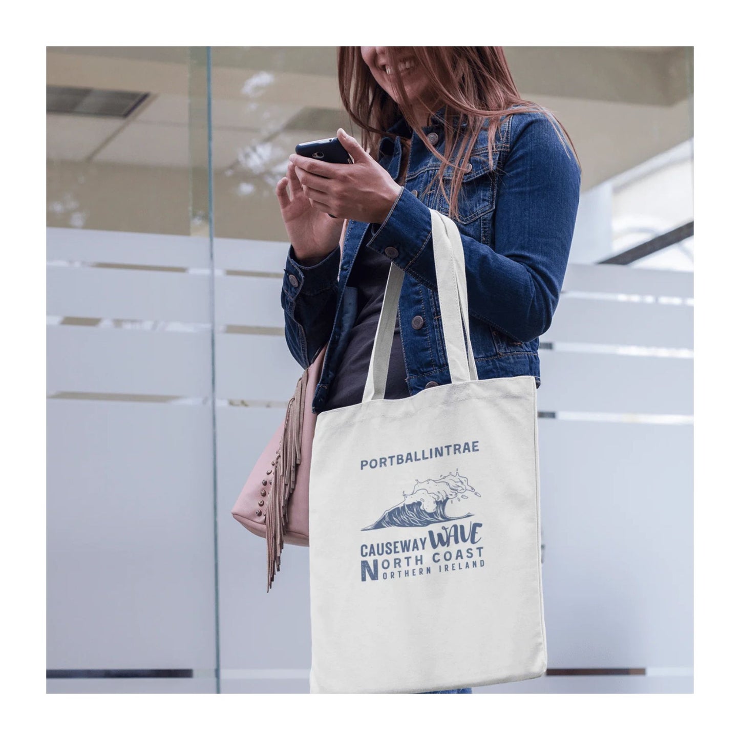Person holding a phone with a tote bag featuring 'Portballintrae Causeway Wave North Coast Northern Ireland' text.