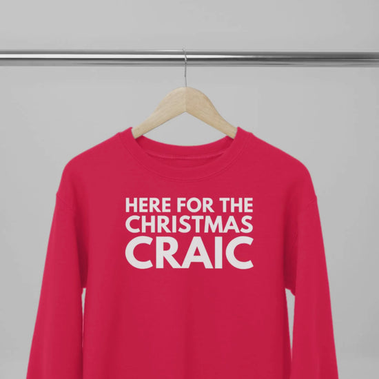 Red sweatshirt with white text 'HERE FOR THE CHRISTMAS CRAIC' on a wooden hanger