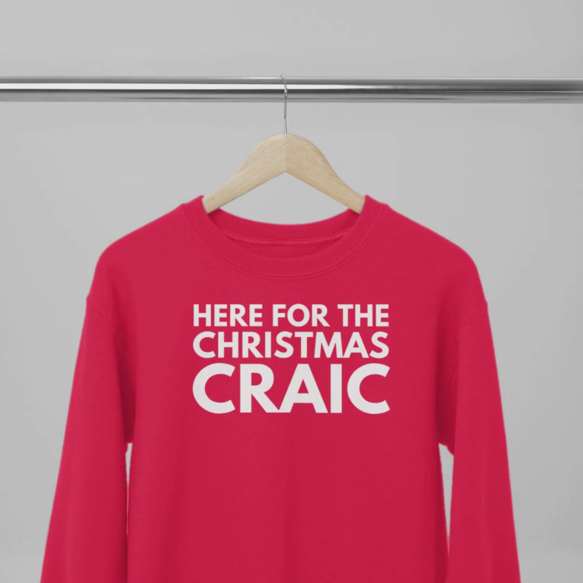 Red sweatshirt with white text 'HERE FOR THE CHRISTMAS CRAIC' on a wooden hanger