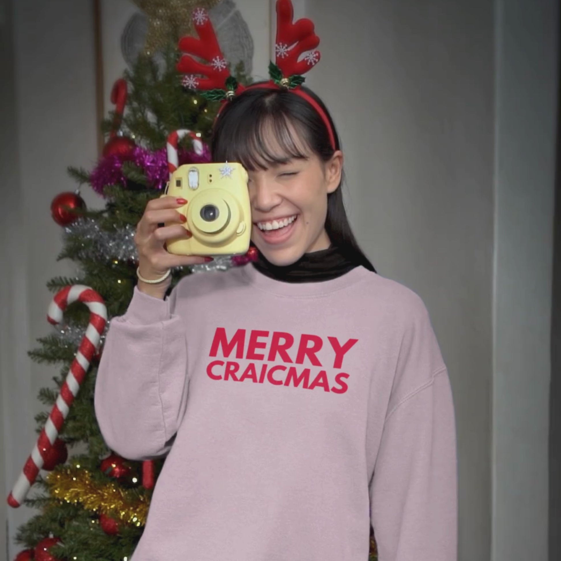 Festive video of girl with a yellow camera wearing pink jumper with red Merry Craicmas text